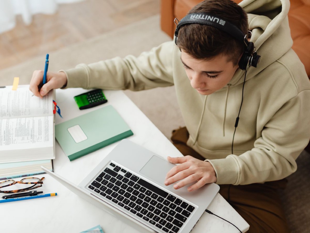 A focused sixth-form student studying Maths online at home, with a laptop, open textbook and calculator at hand.